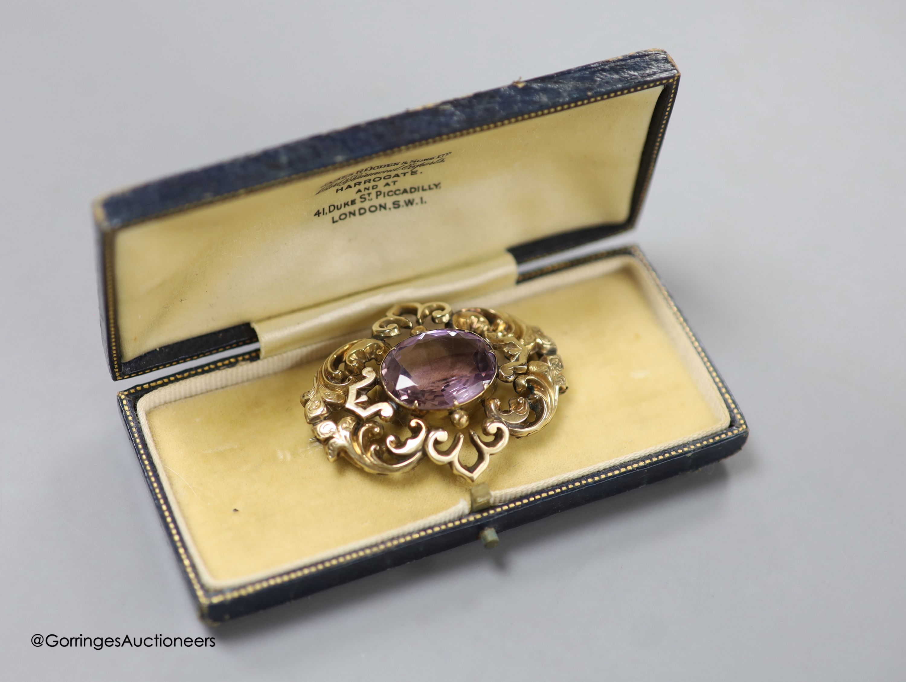 A cased late Victorian yellow metal and amethyst set pierced scroll brooch, 45mm